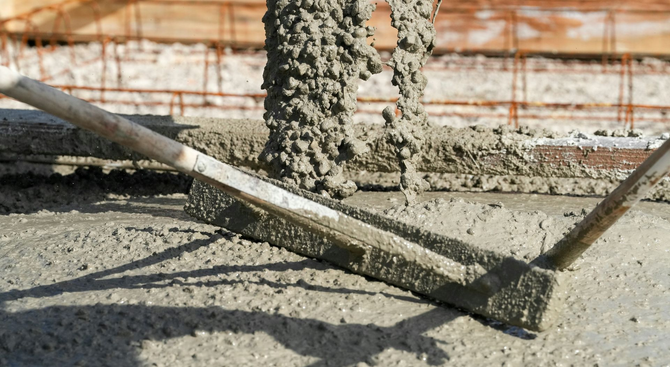 Wet concrete being poured and leveled with a hand tool at a construction site.