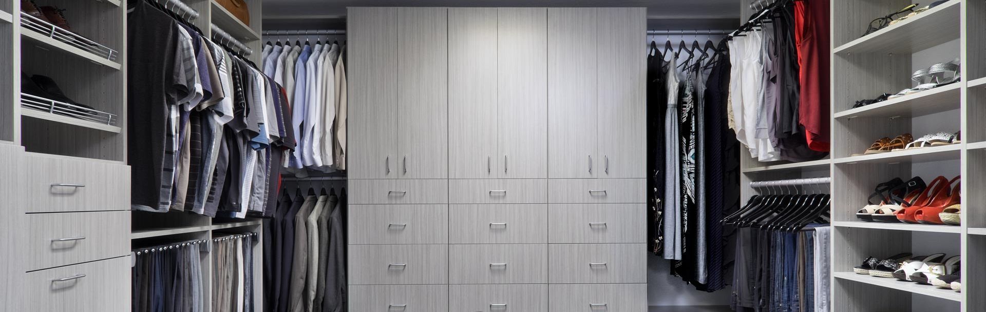 A walk-in closet with a shoe rack and chair. Closet cabinet filled with clothes and shoes, and an island seat.