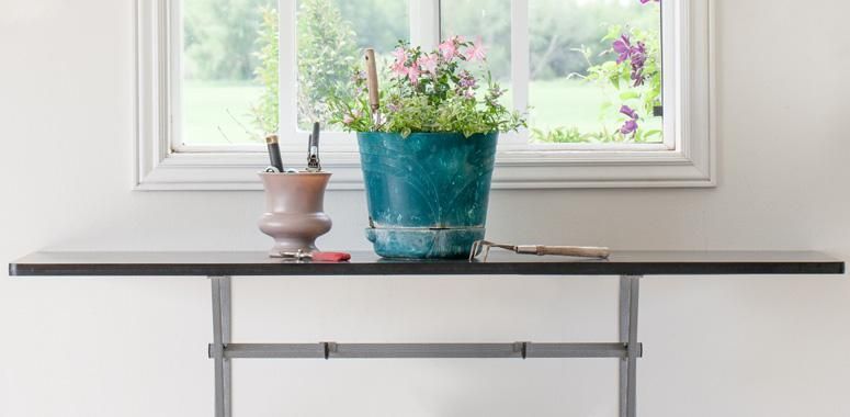 a vase of flowers is sitting on a folding workbench in front of a window .