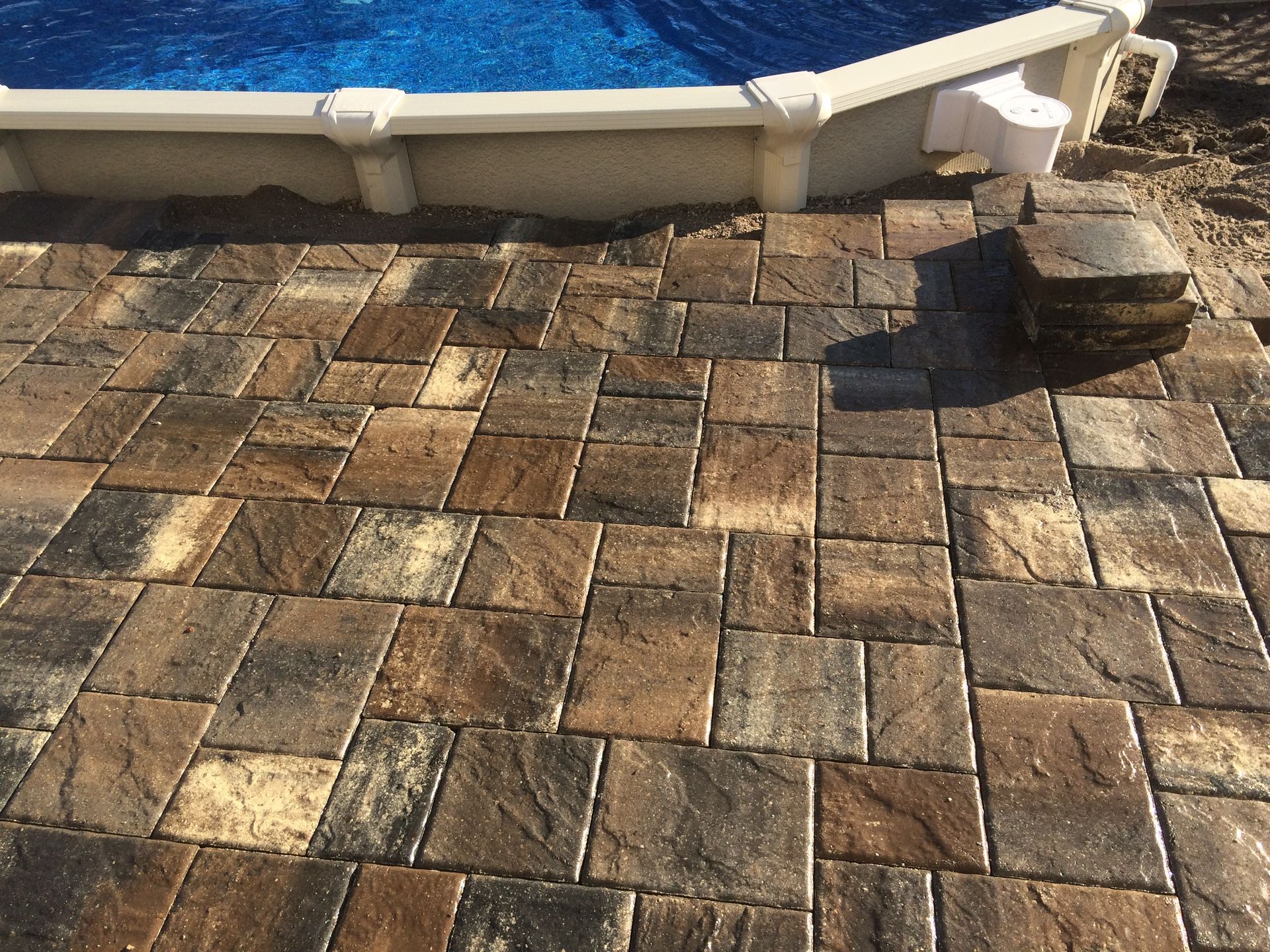 A patio with bricks and a pool in the background