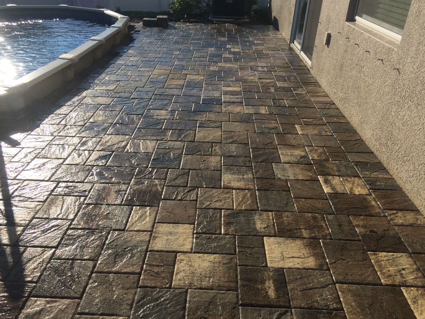 A brick walkway leading to a pool next to a building.