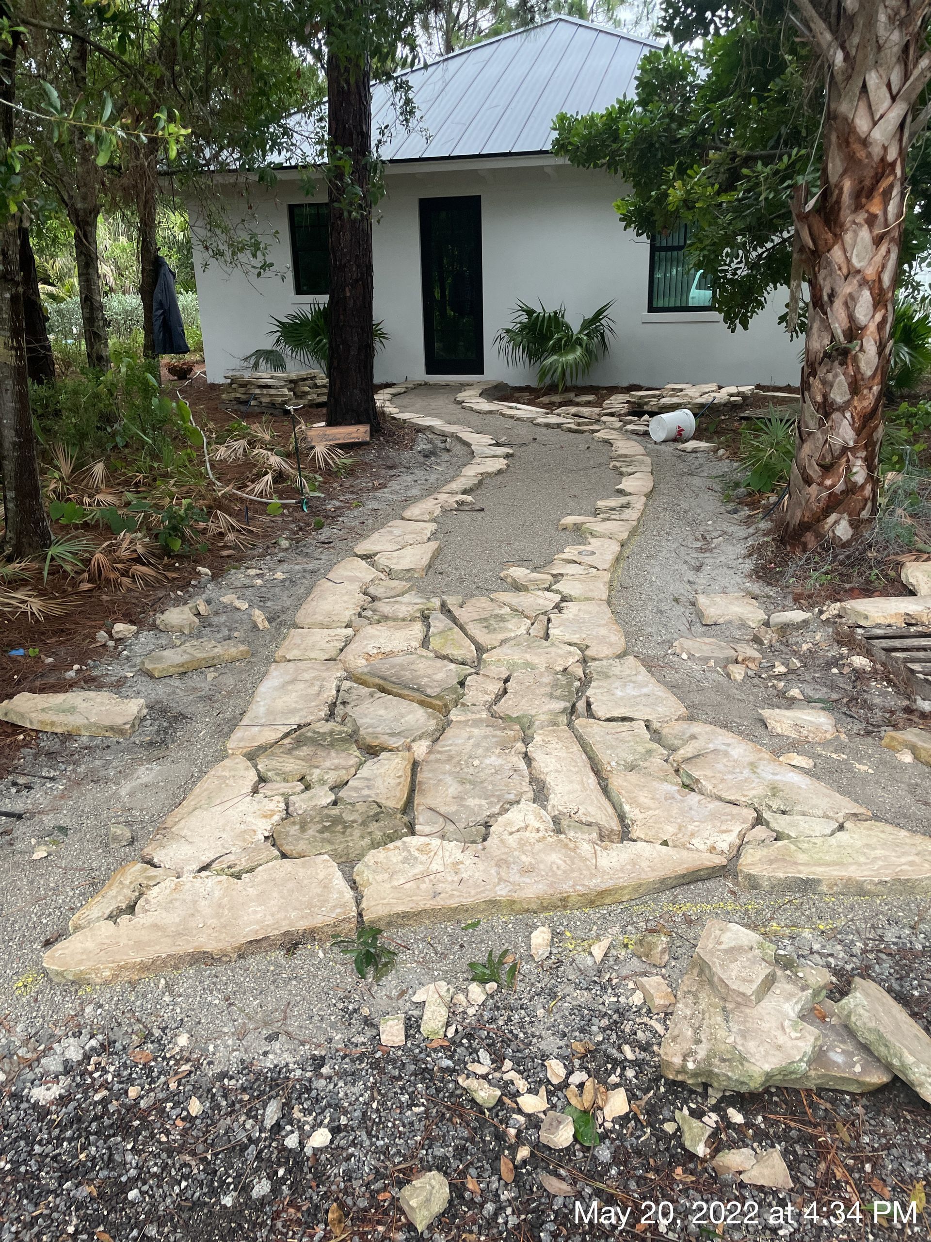 A stone walkway leads to a white house surrounded by trees.