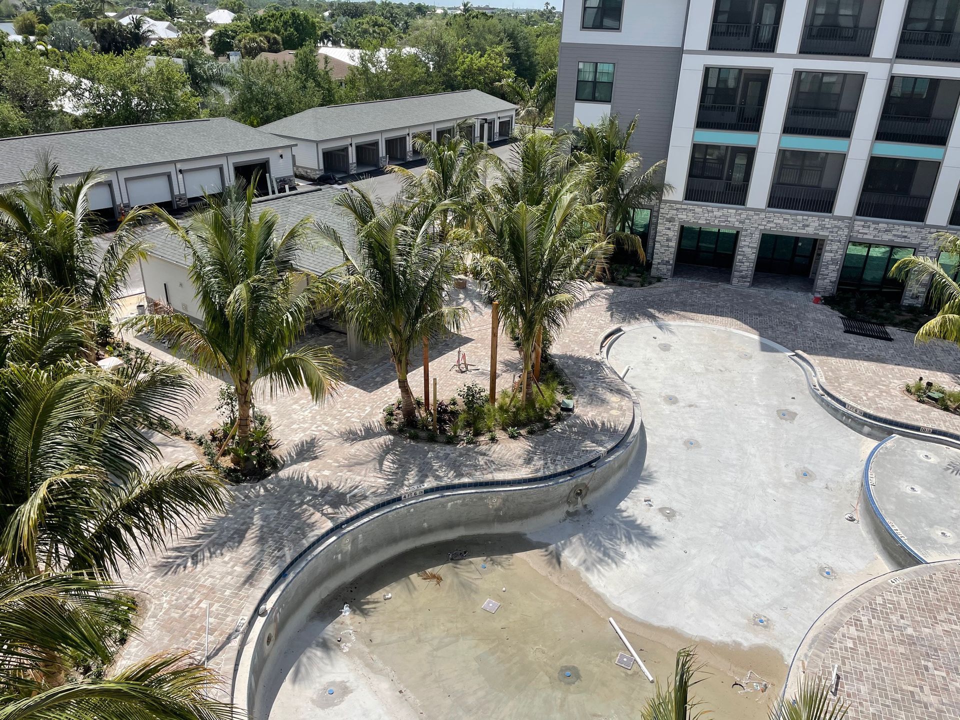 An aerial view of a swimming pool in front of a building surrounded by palm trees.