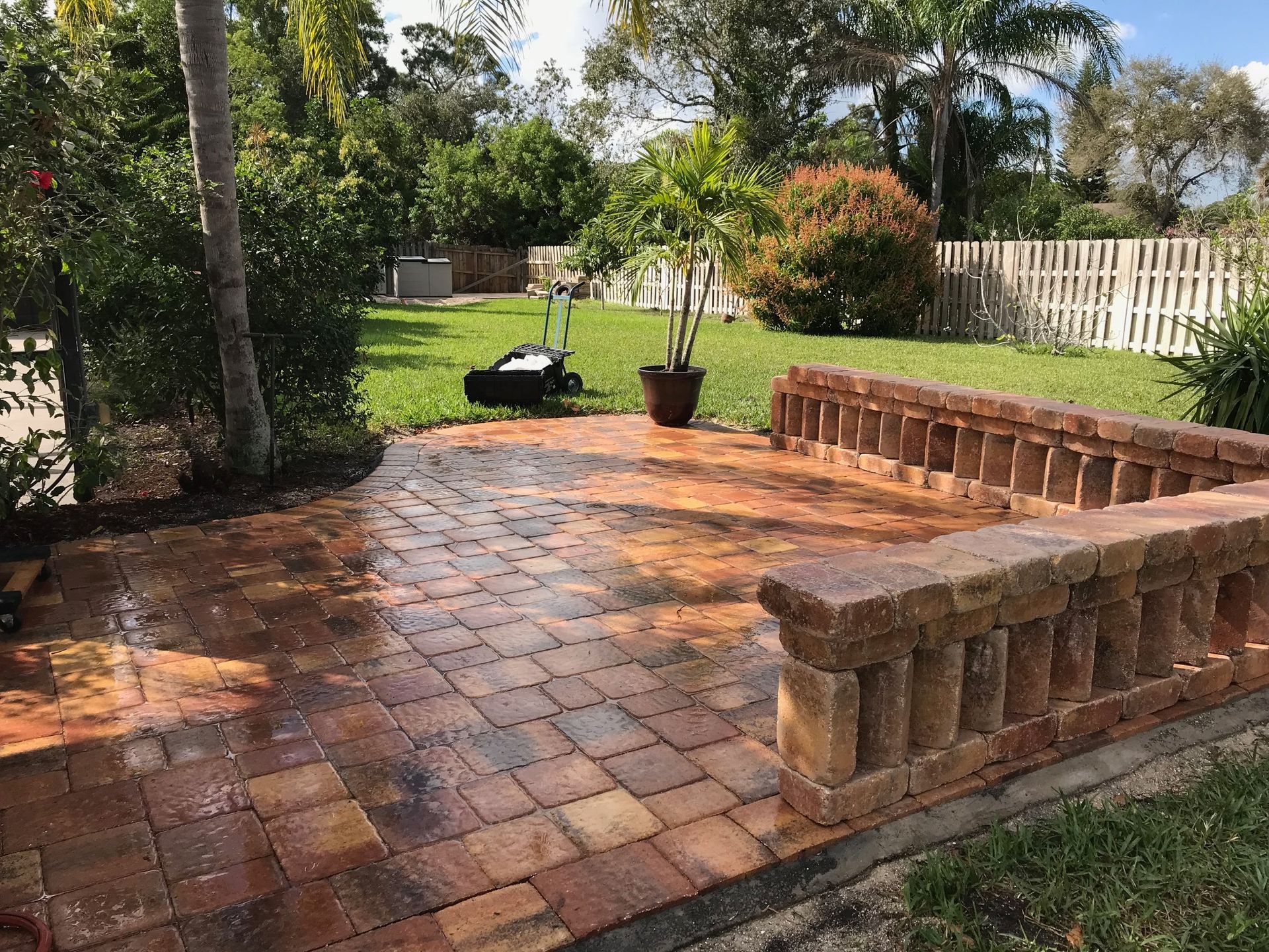 A brick patio with a bench and a fence in a backyard.