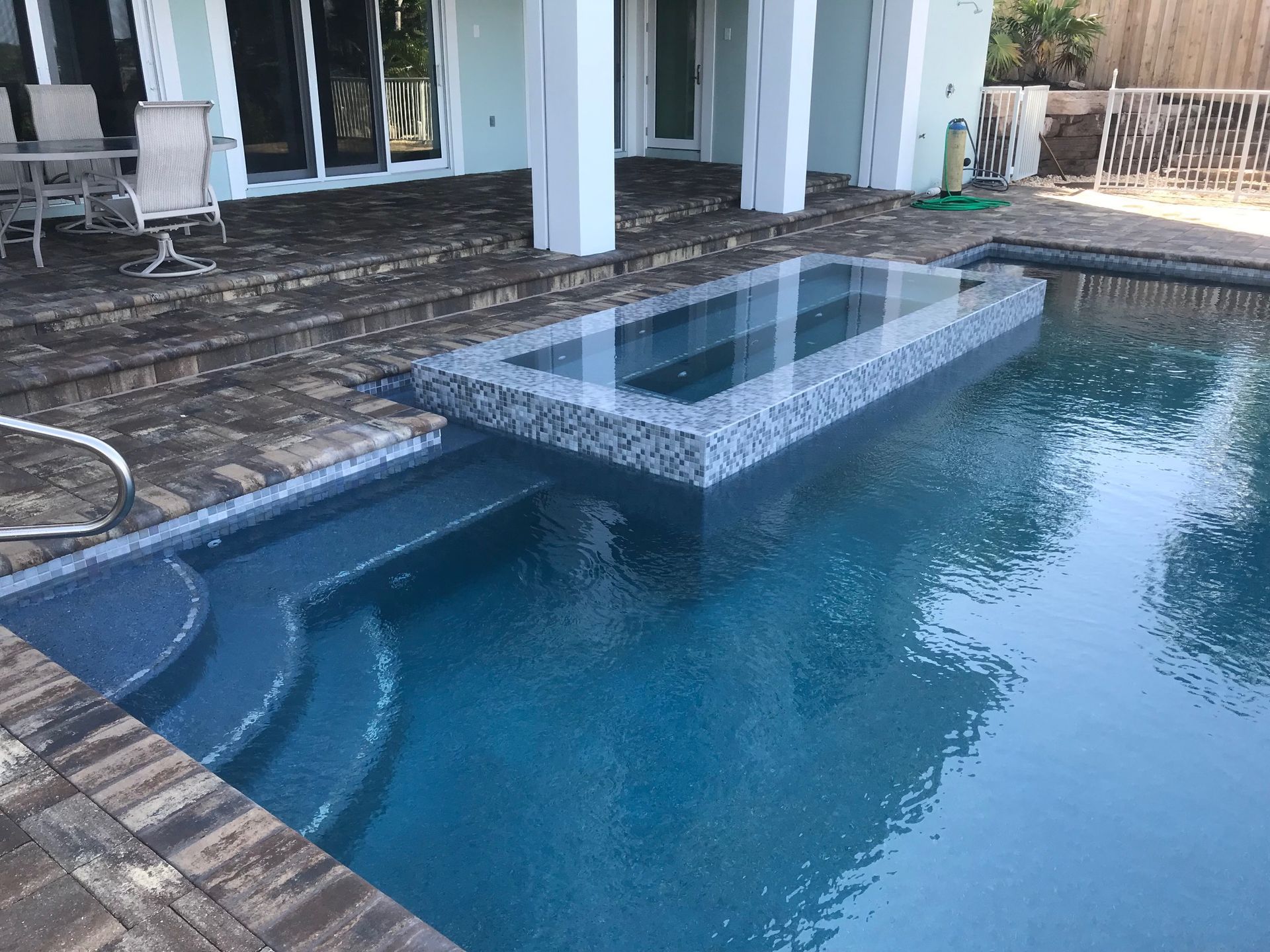 A large swimming pool with stairs leading up to it is in the backyard of a house.