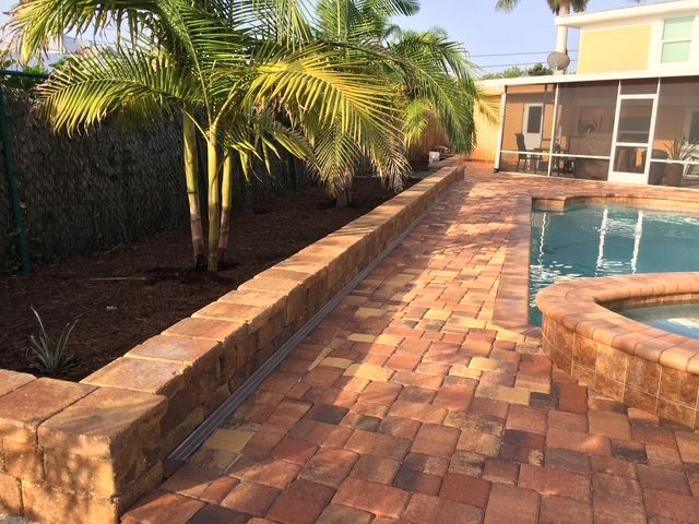 A brick walkway leading to a swimming pool surrounded by palm trees