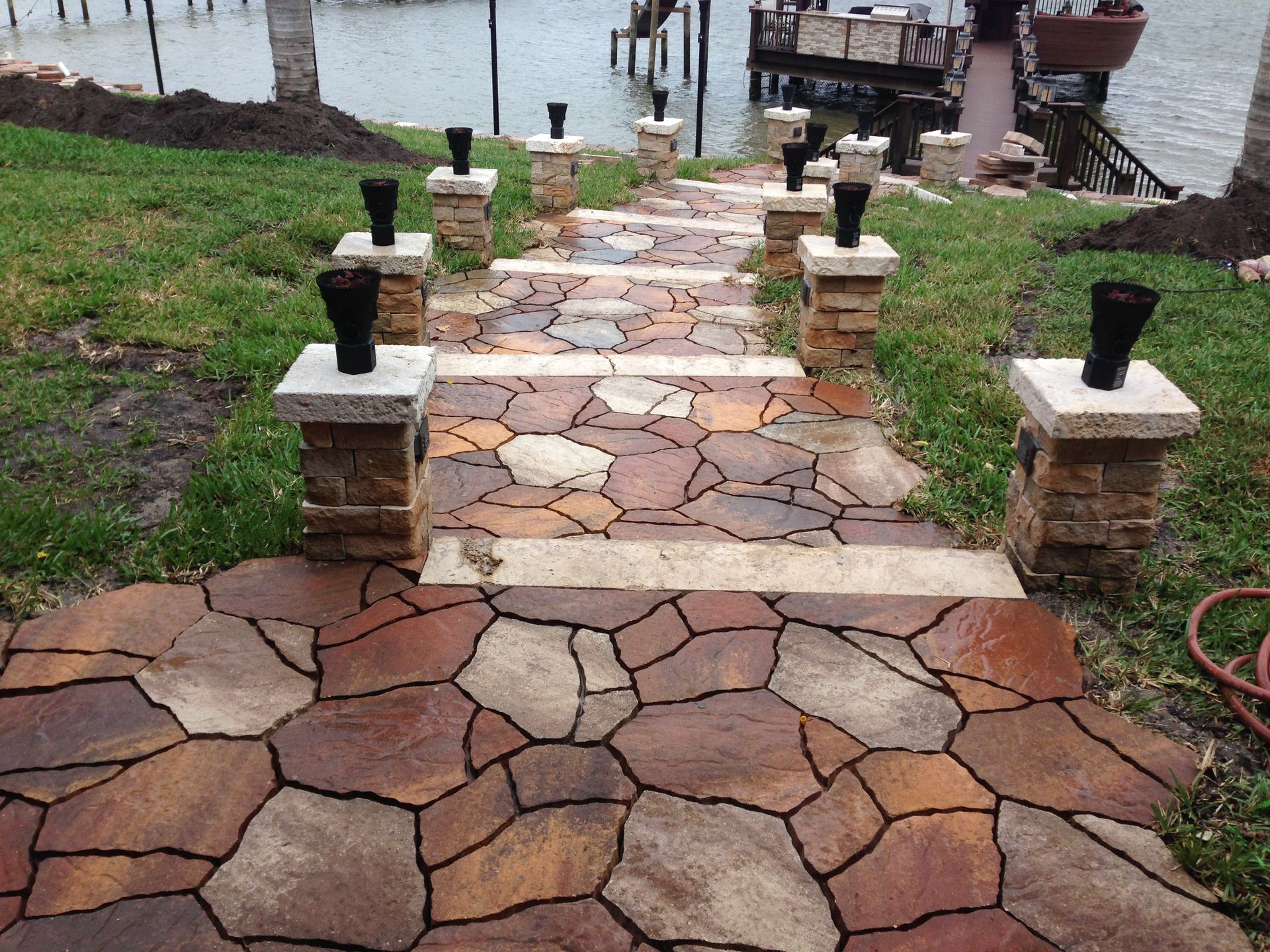 A stone walkway leading to a lake with a dock in the background.