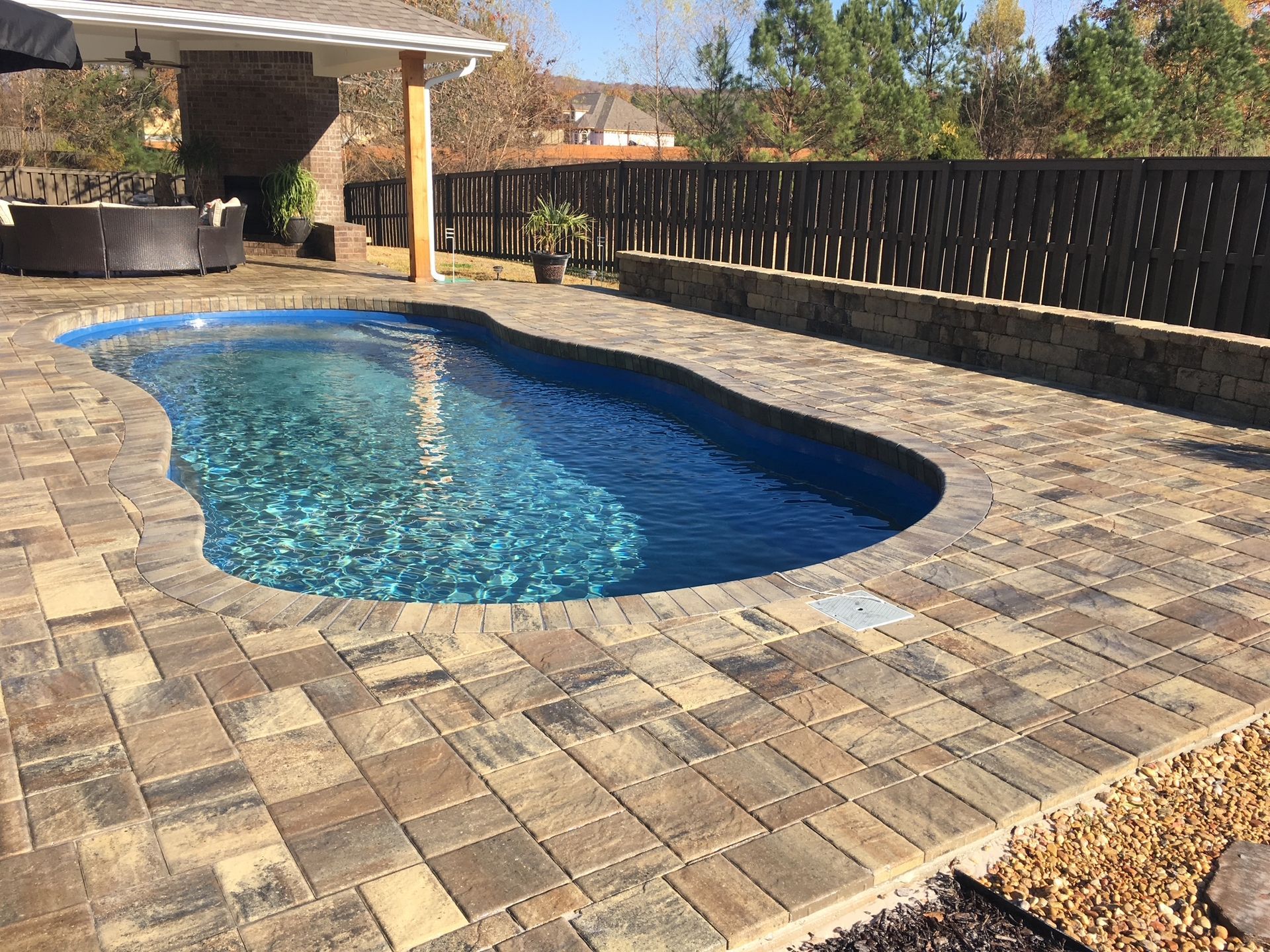 A large swimming pool is surrounded by a brick patio.