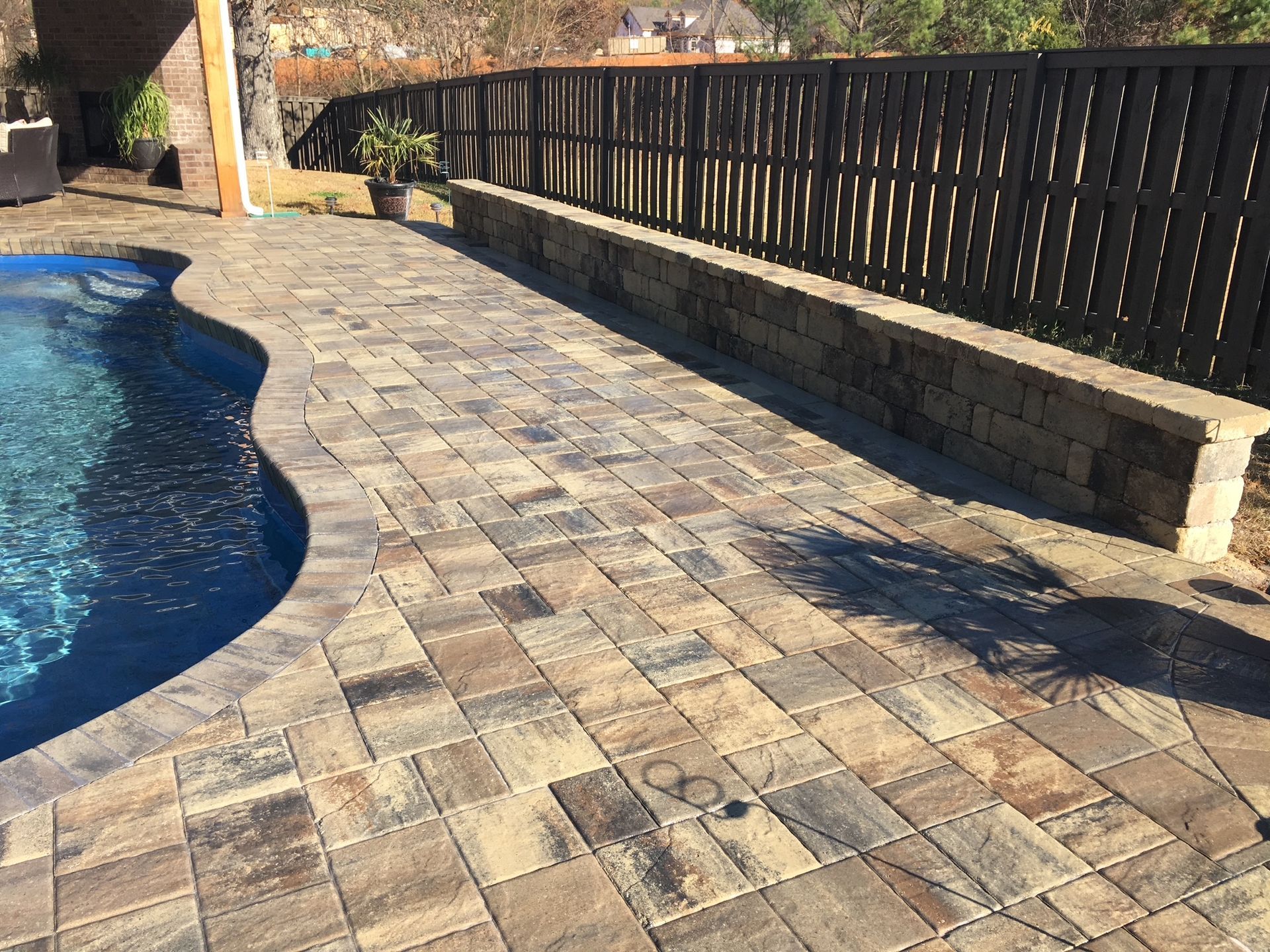 A brick patio next to a swimming pool with a black fence.