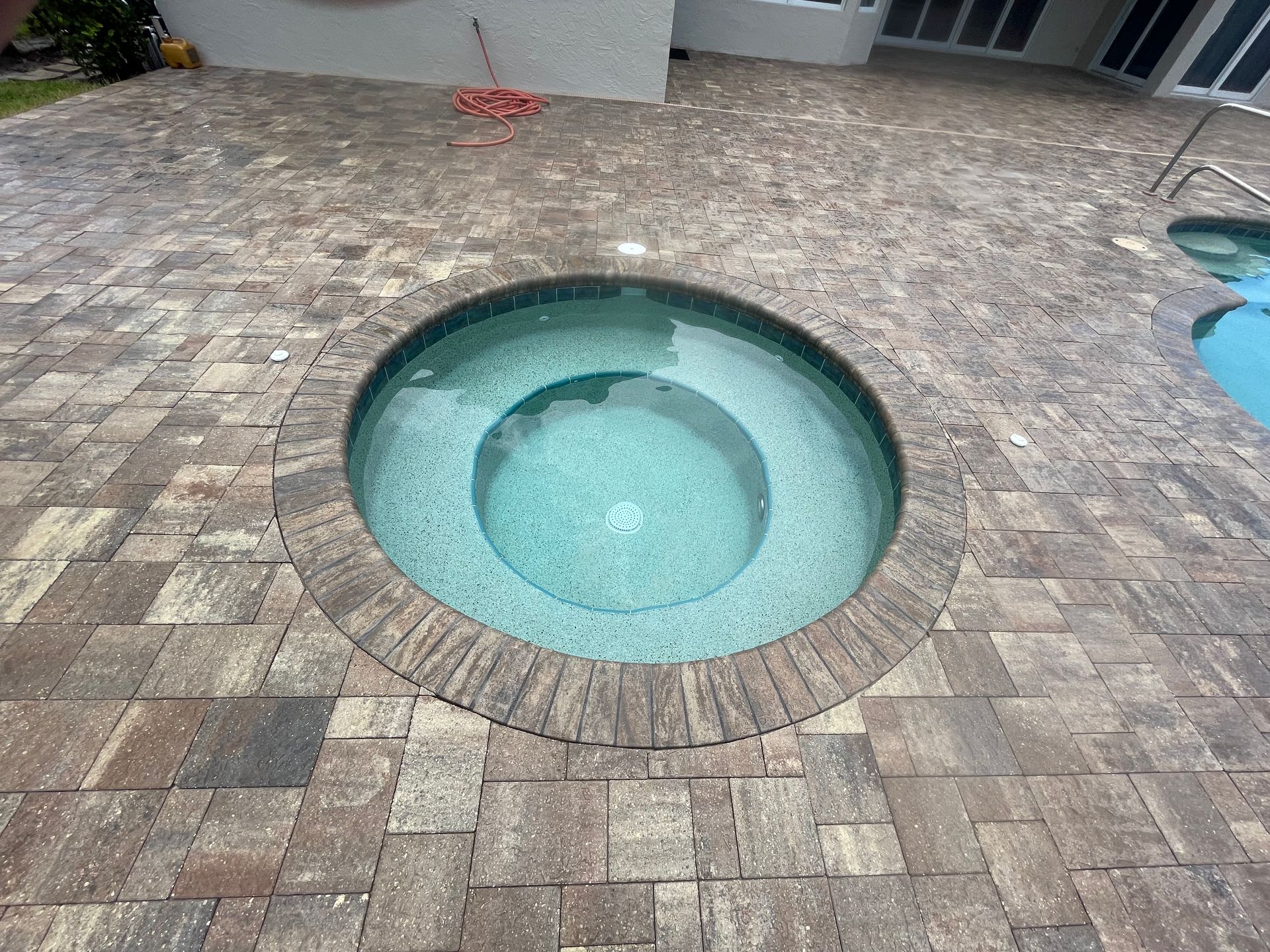 A hot tub in the middle of a brick patio next to a swimming pool.