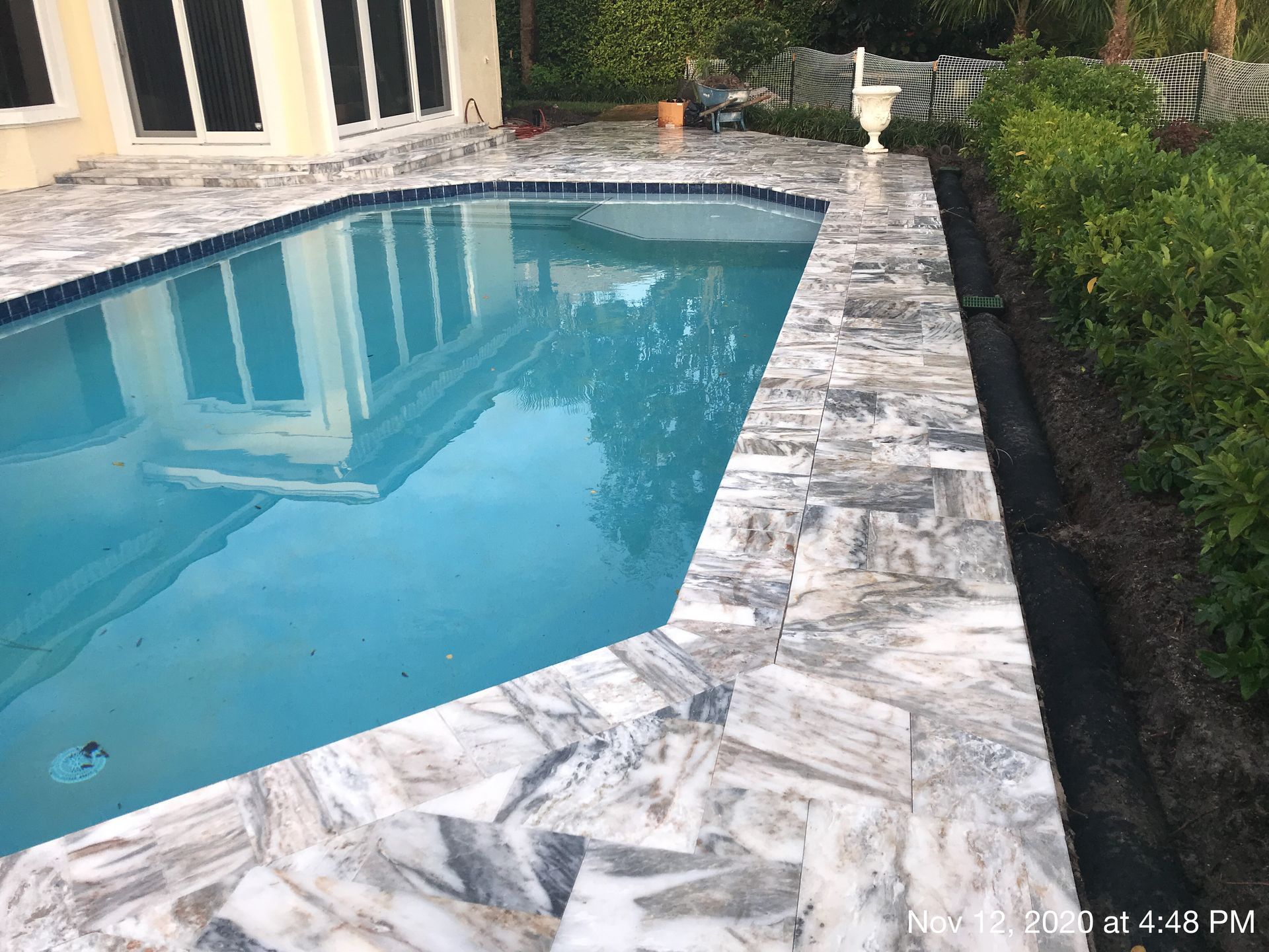 A large swimming pool with a tiled patio in front of a house.