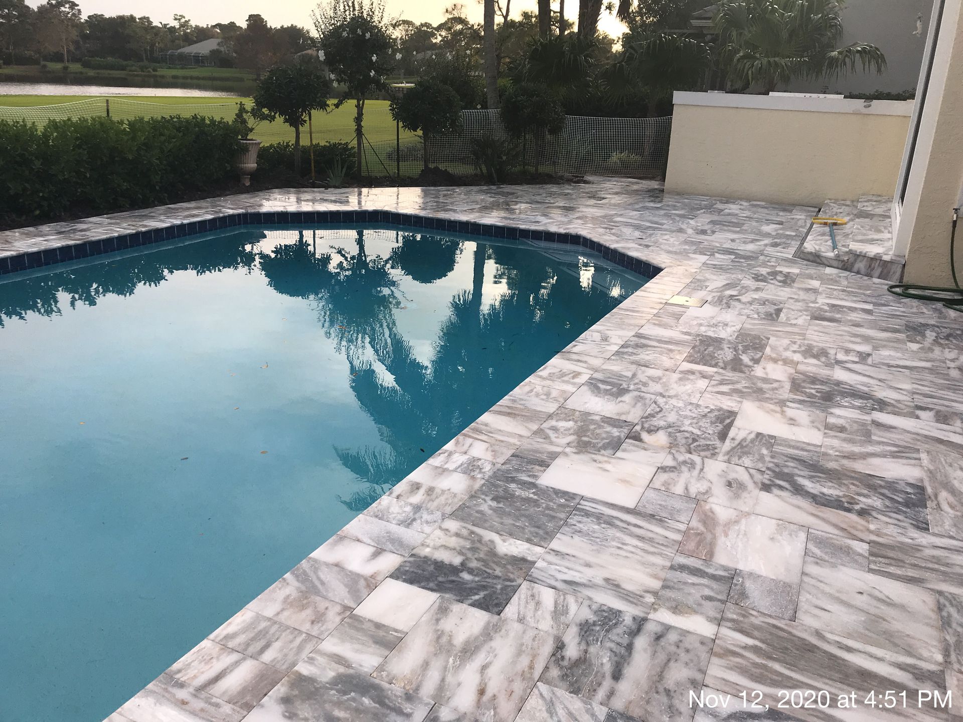 A large swimming pool is surrounded by a tiled patio.