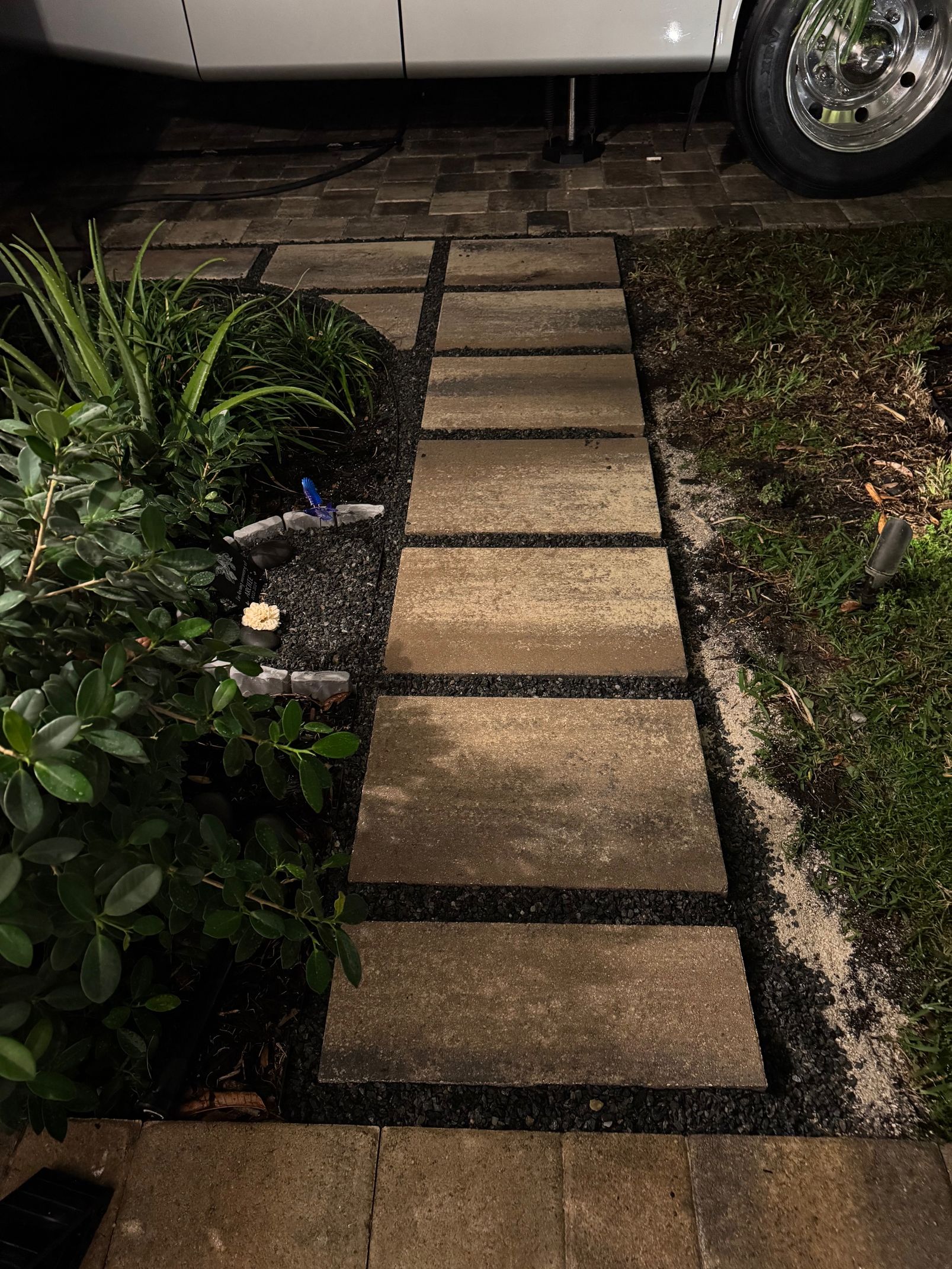A brick walkway leading to a white van is lit up at night.