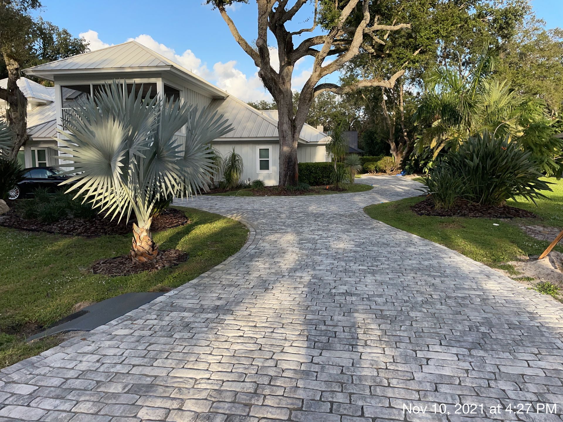 A brick driveway leading to a house with palm trees.