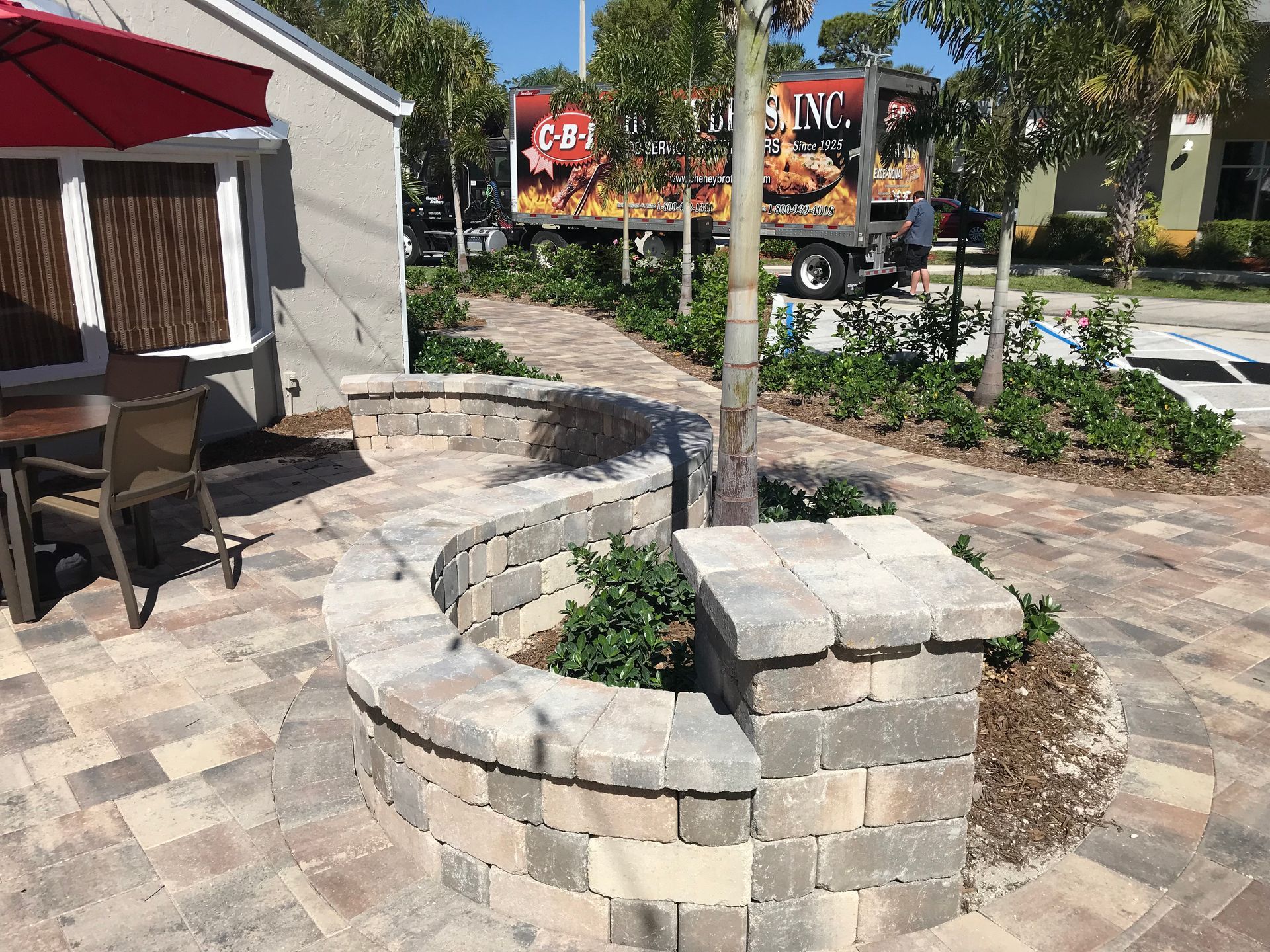 A patio with a table and chairs and a red umbrella in front of a restaurant.