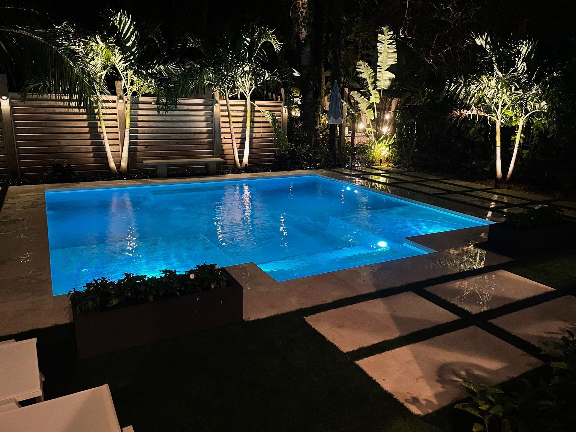 A large swimming pool is lit up at night in a backyard.