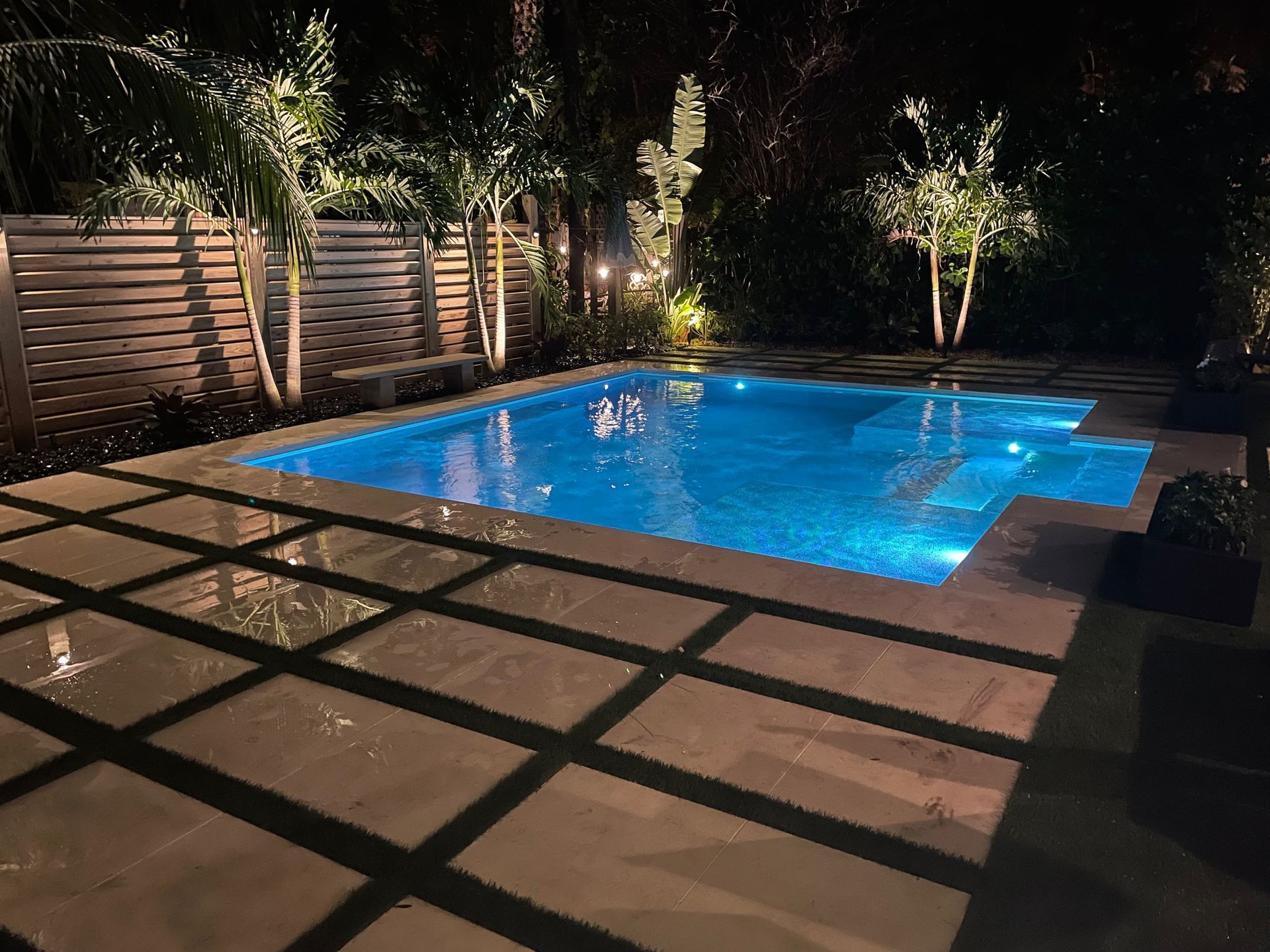 A large swimming pool is lit up at night in a backyard.
