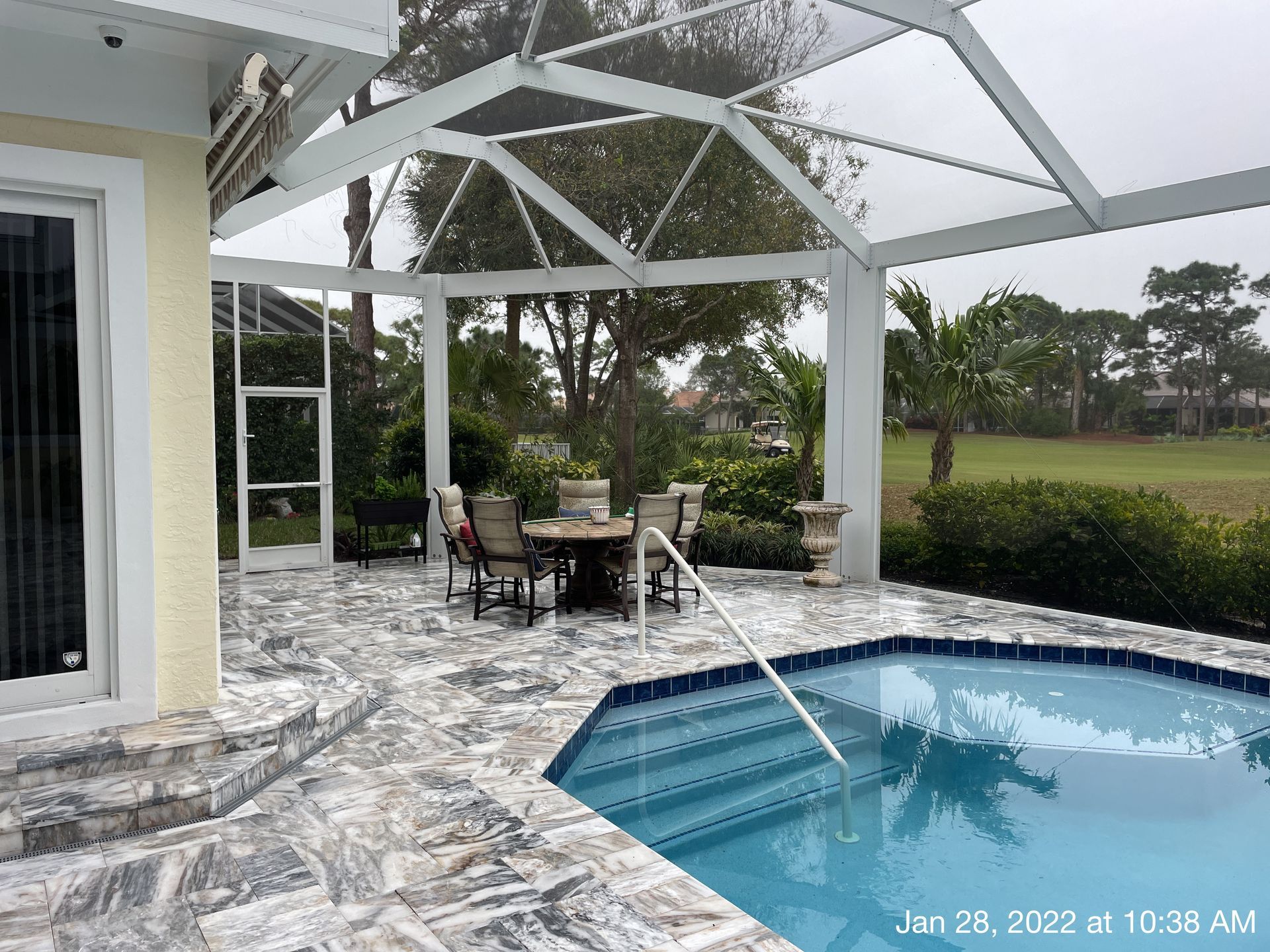 A swimming pool is surrounded by a screened in area with a table and chairs.