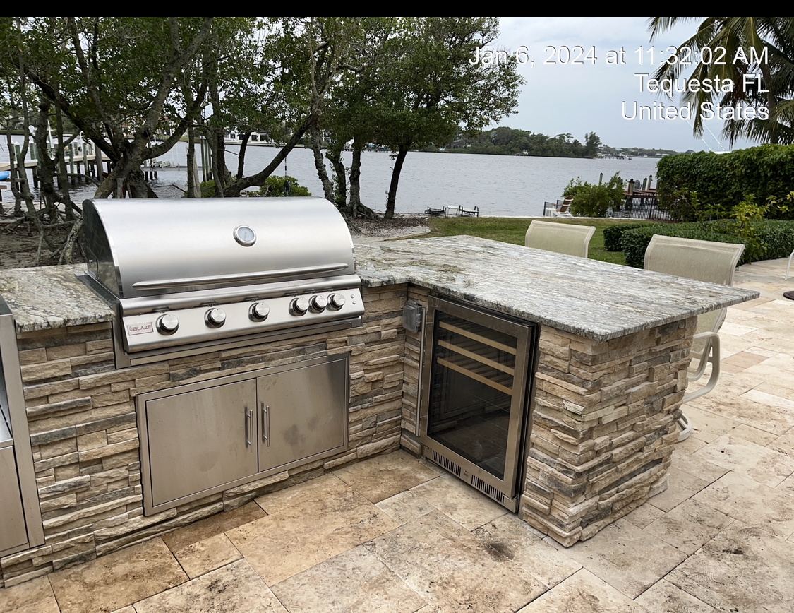 An outdoor kitchen with a grill and a refrigerator.