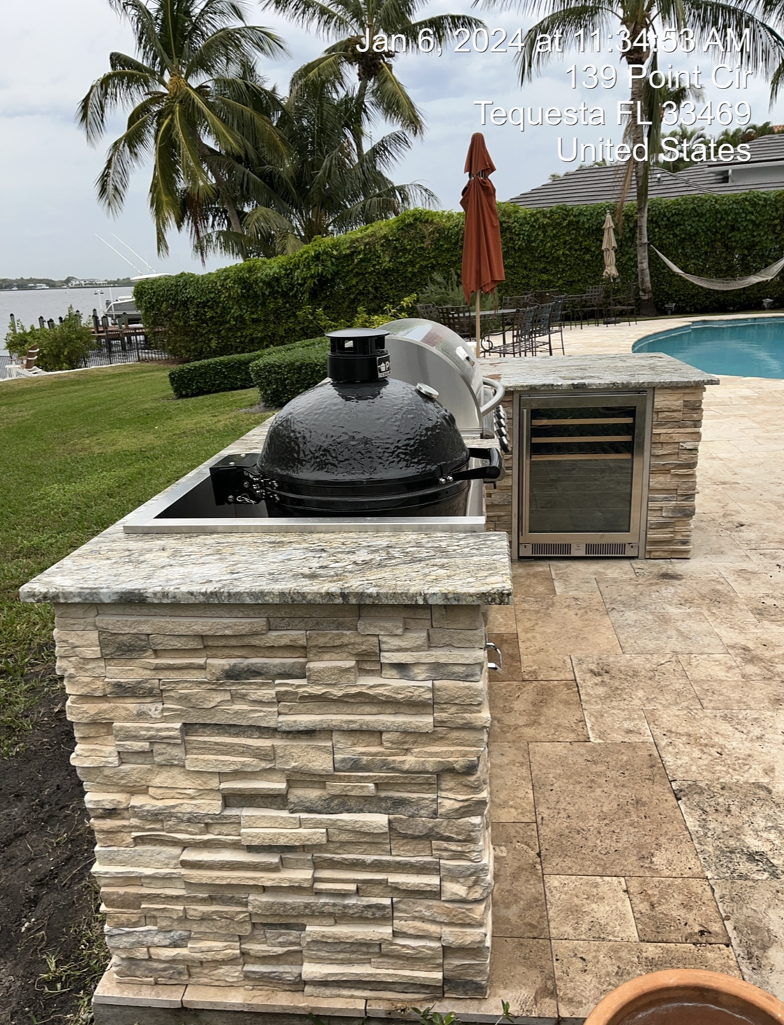 A grill is sitting on top of a stone pillar next to a pool.