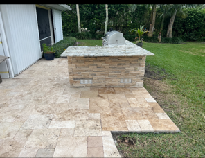 A patio with a grill and a stone counter top in the backyard.