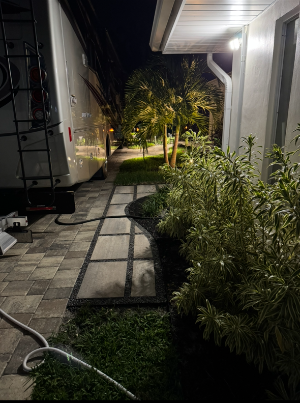 A sidewalk leading to a house at night with a trailer parked next to it.