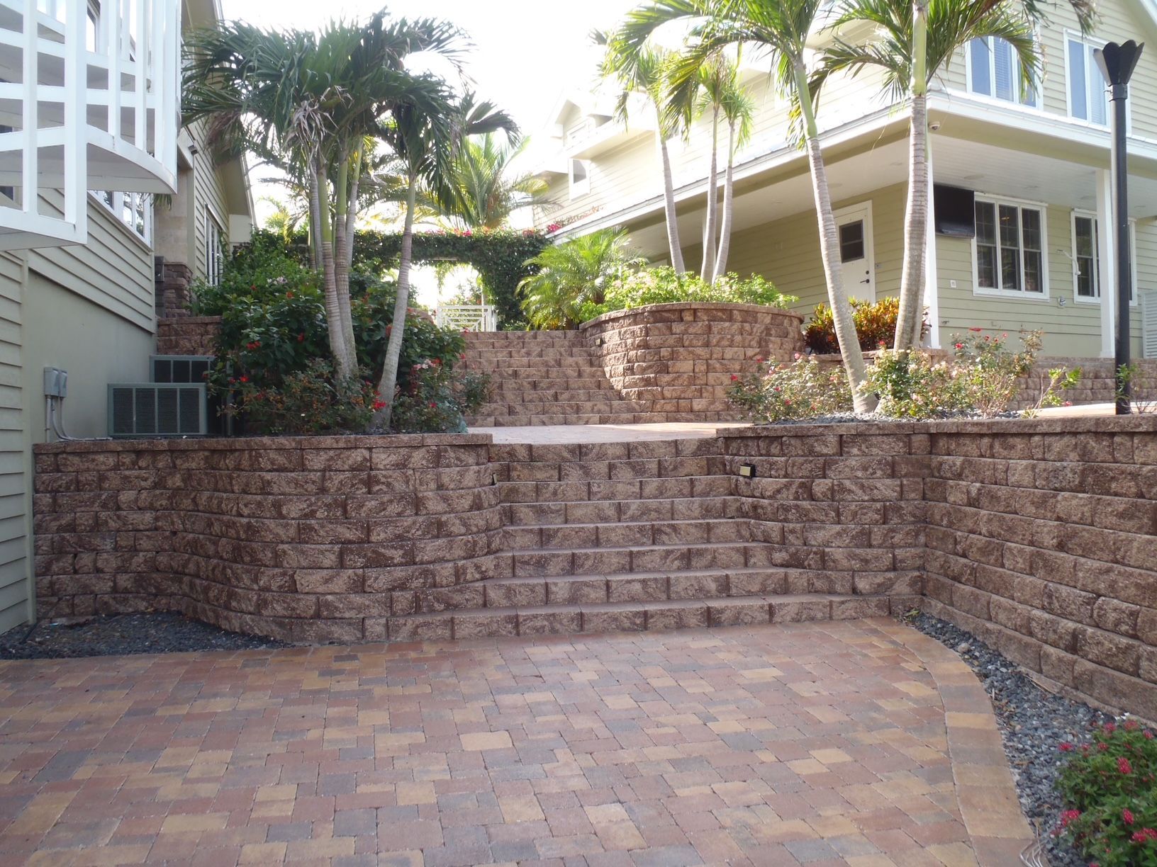 A brick wall with stairs leading up to a house with palm trees in the background.