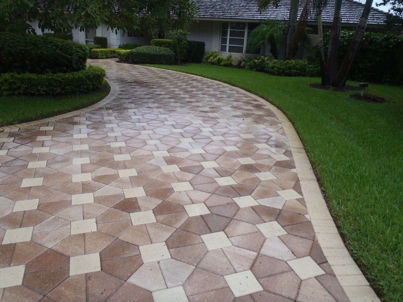 A brick driveway leading to a house with a lush green lawn
