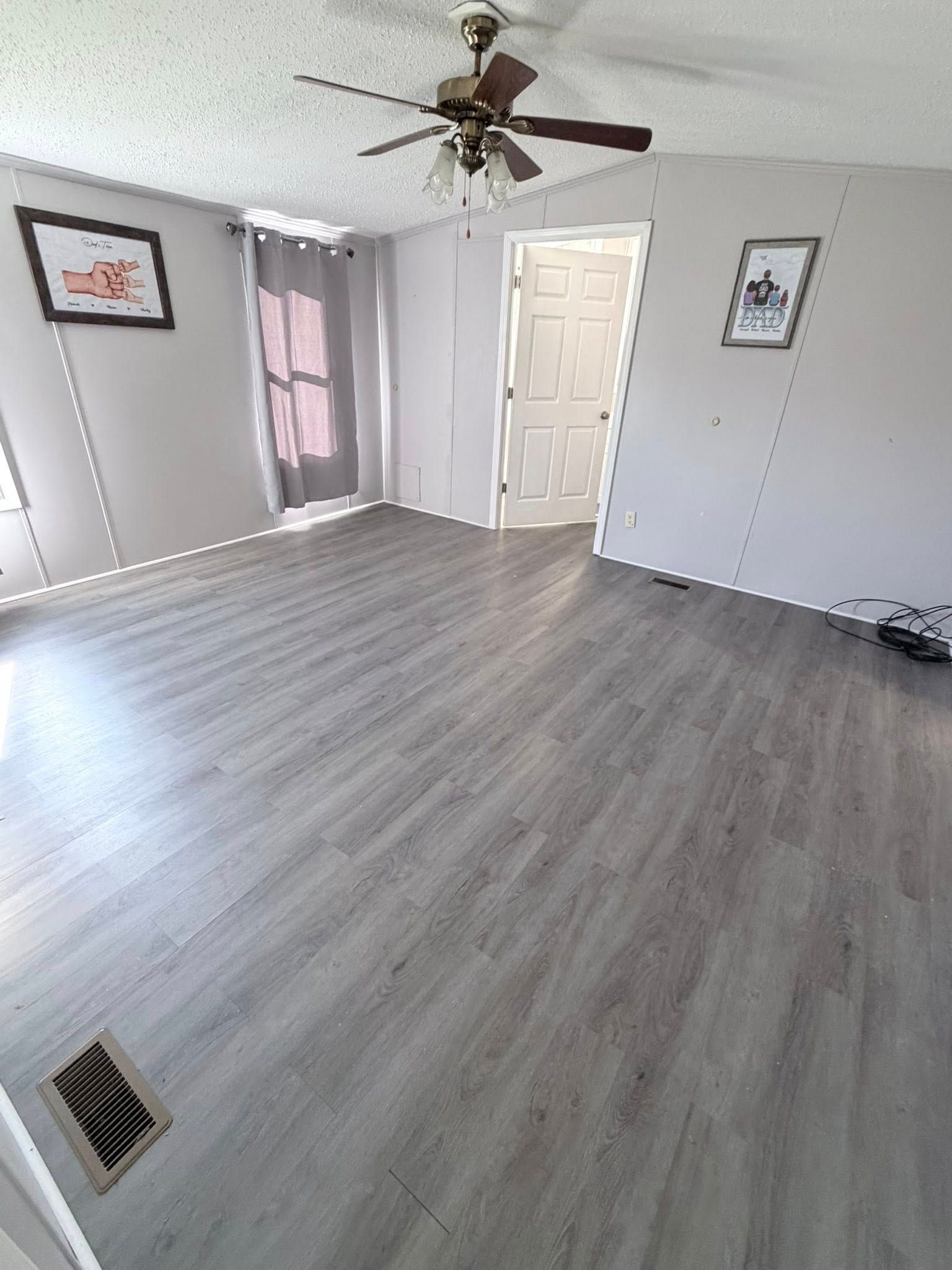 Empty bedroom with gray wood flooring, white walls, ceiling fan, and two framed pictures.