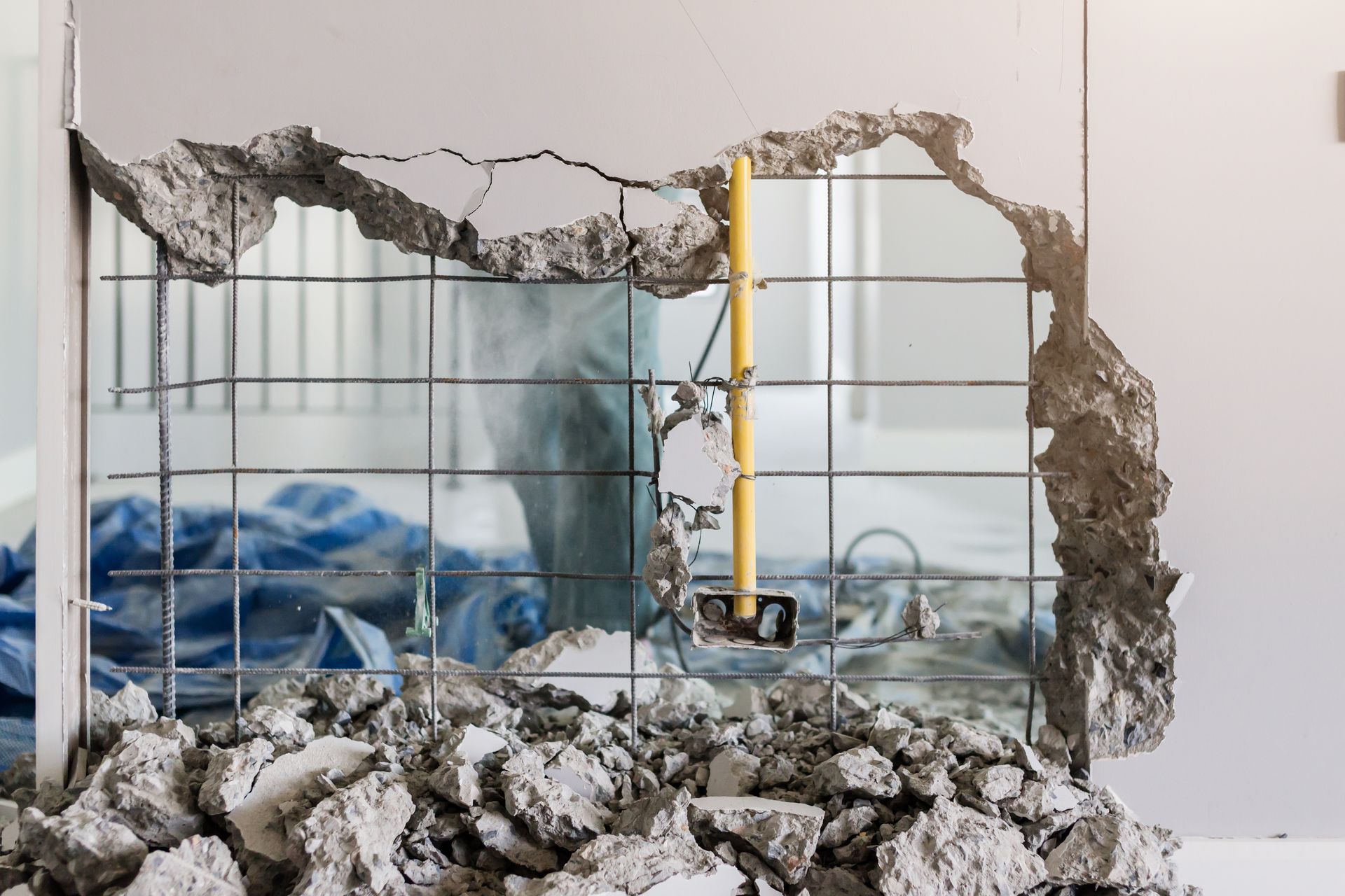 Damaged wall with a large hole, exposing a messy room with a blue bed and metal frame inside.