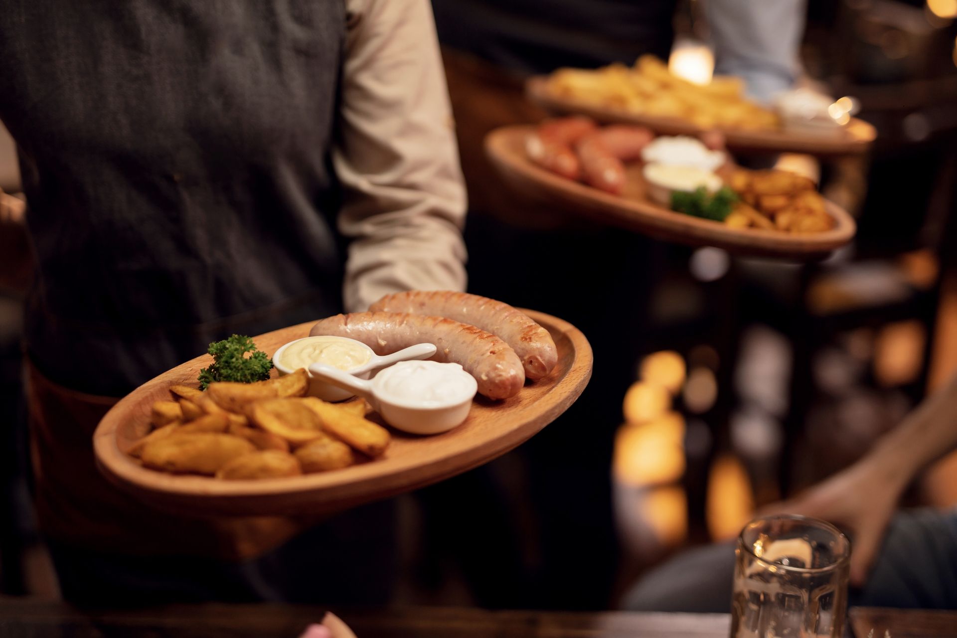 Waiters carrying wooden platters of sausage, fries, and condiments