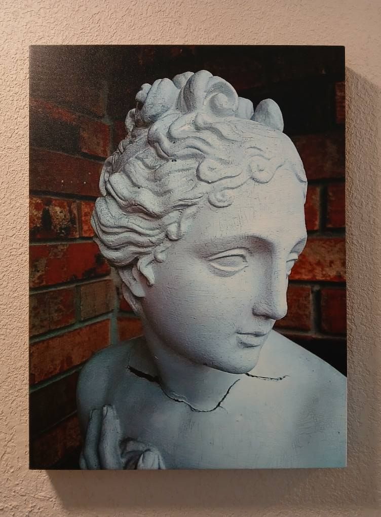White bust statue against a brick wall. The statue has curly hair and is looking down.