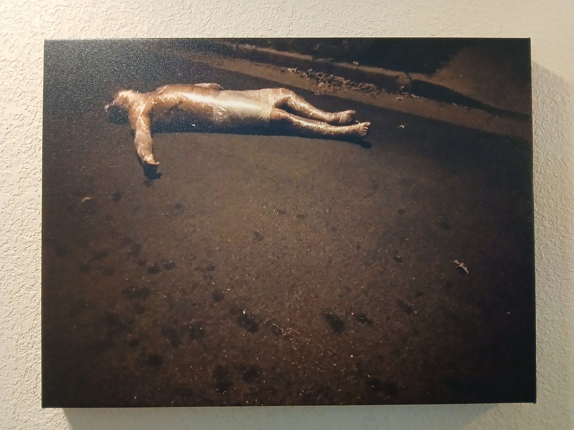 A person lies prone on a dark surface, possibly a beach, appearing still.