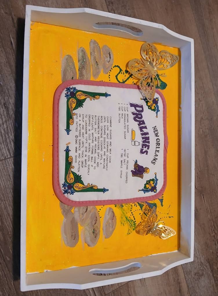 Tray with a yellow background, featuring a New Orleans praline recipe, gold butterflies, and a white rim.