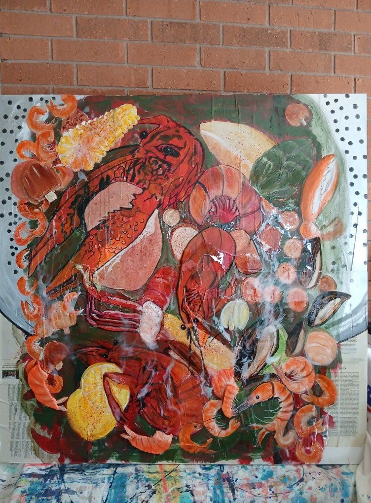 Overhead view of a colorful crawfish boil art piece on metal. Red crawfish, corn, and shrimp are arranged on a green surface.