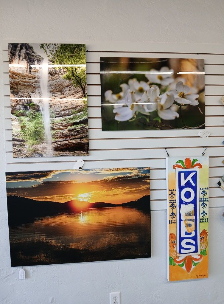 Wall display of landscape art: waterfall, white flowers, sunset over water, and a decorative sign.