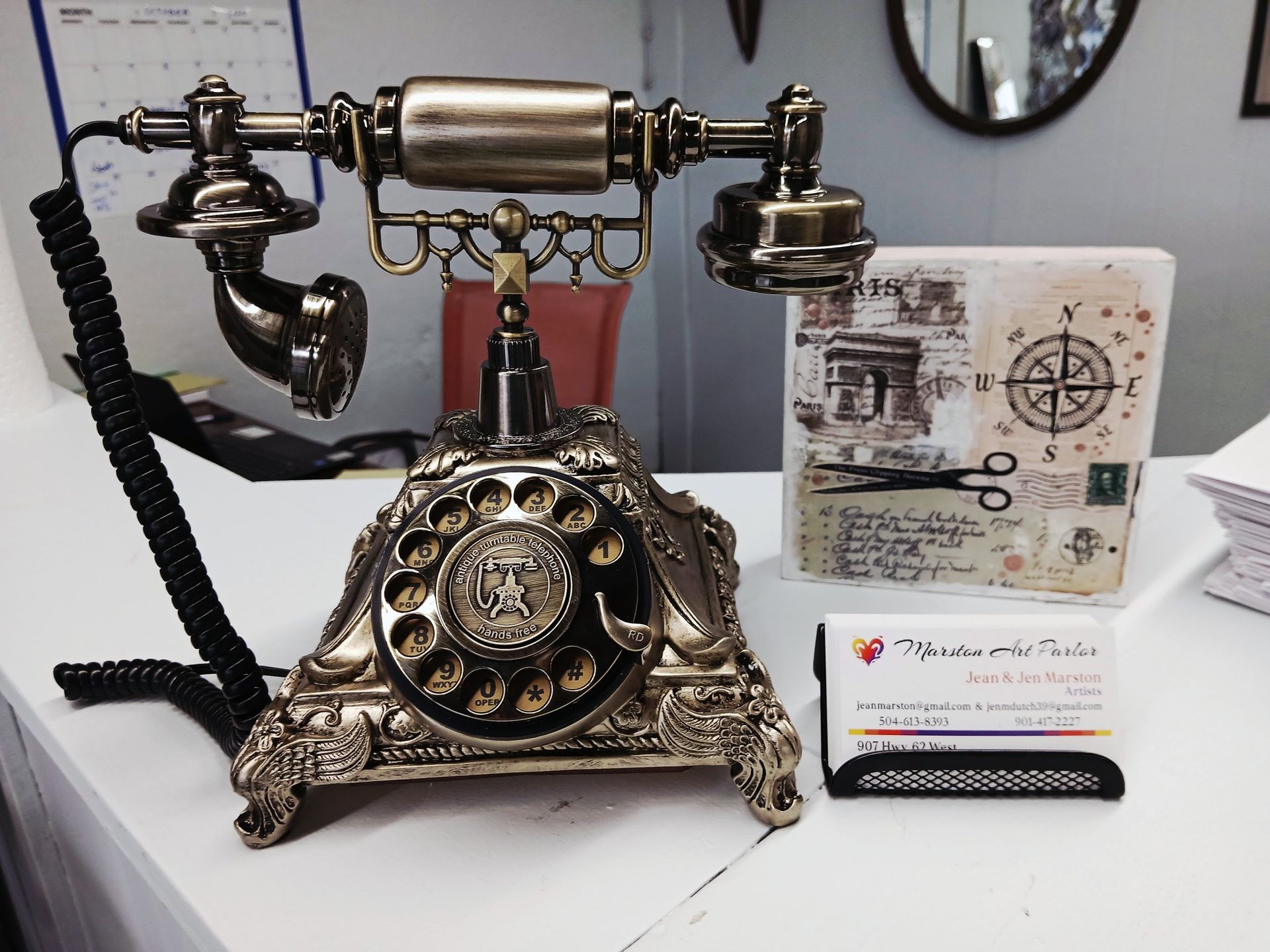 Antique rotary phone on a white surface, next to a business card holder and decorative block with scissors.