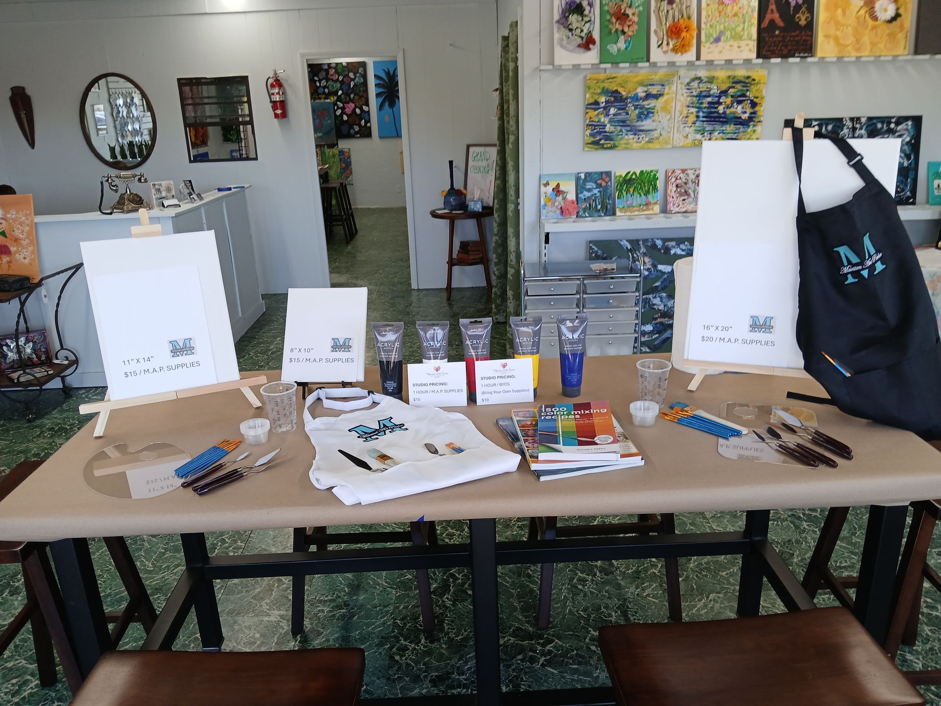 Art supplies arranged on a table: canvases, brushes, paint, and an apron inside a studio.