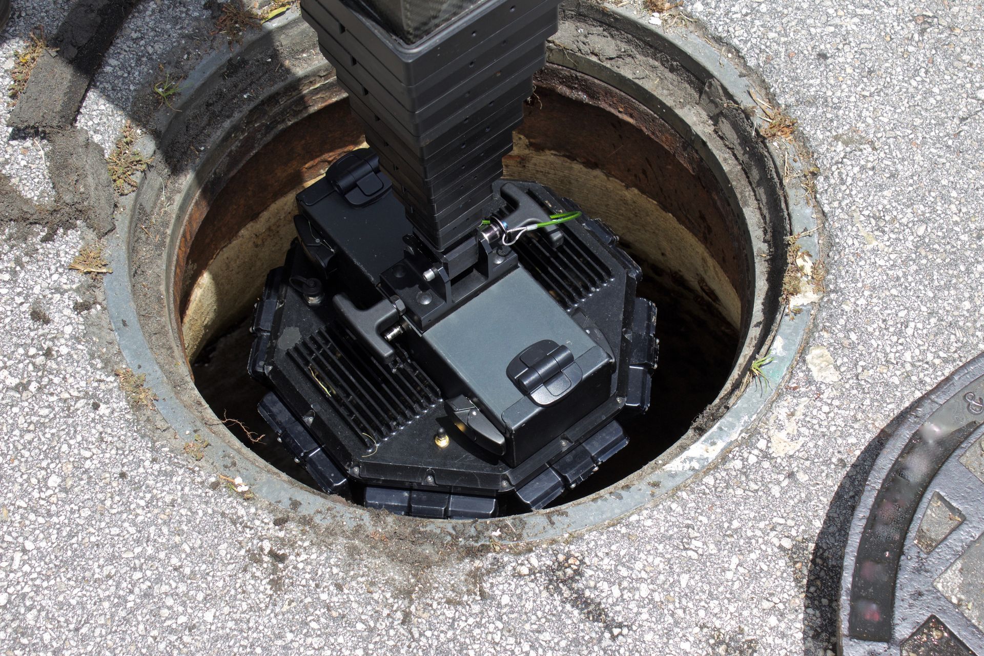 Robot inside a manhole; black device with multiple square sections, positioned in a concrete ring.