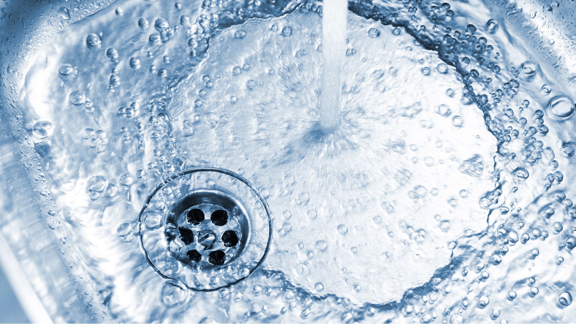 Water flowing into a stainless steel sink, splashing around the drain. Water flowing into a stainless steel sink, splashing around the drain.