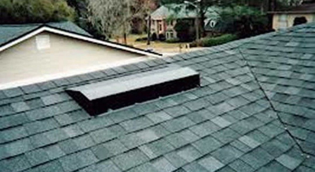 Dark asphalt shingle roof with a vent and a portion of a building.