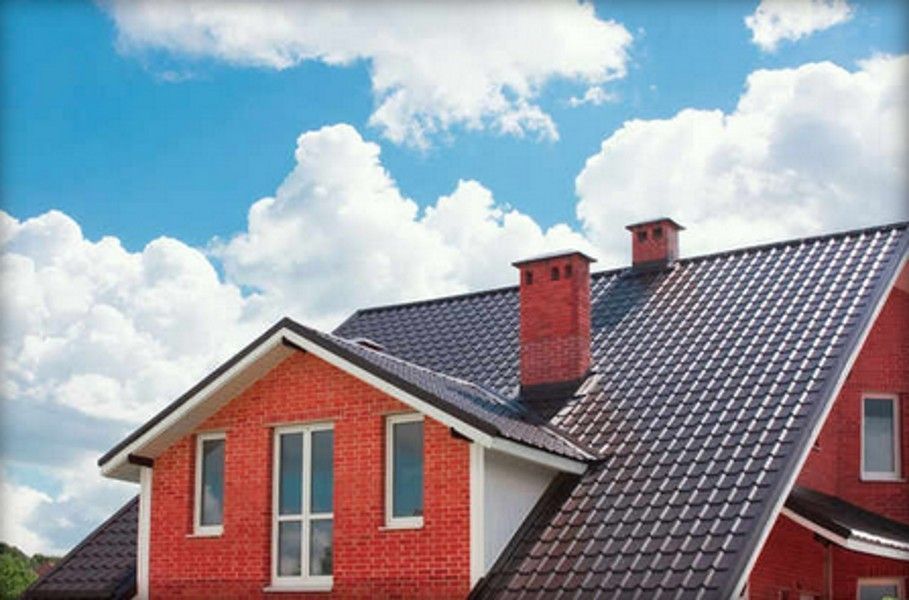 Red brick house with dark brown roof, chimneys, and blue sky with clouds.
