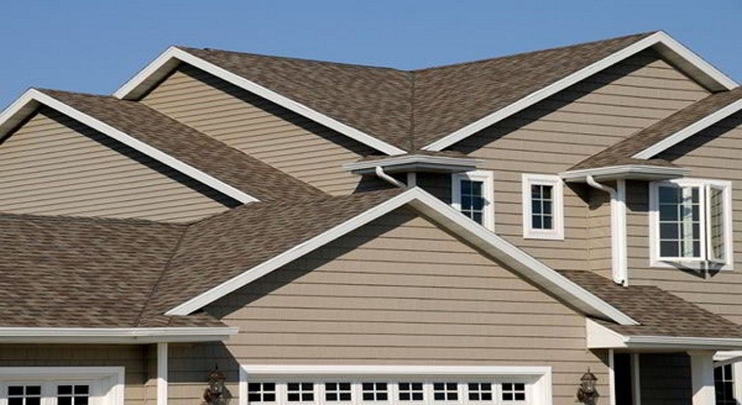 Beige house with multiple roof gables, white trim, and brown shingles.