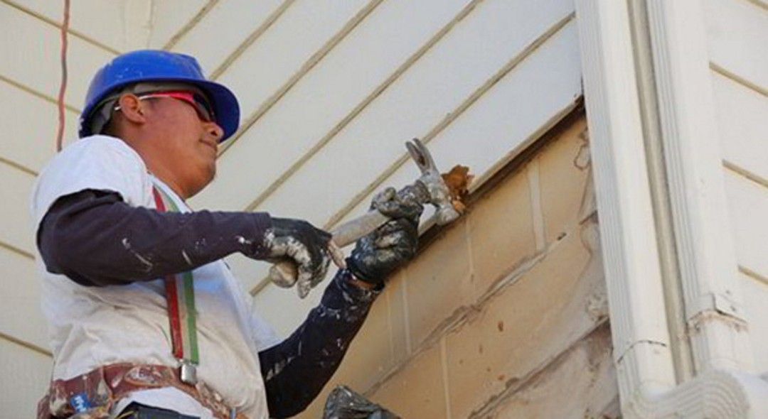 Construction worker in blue hard hat caulking siding on a house.