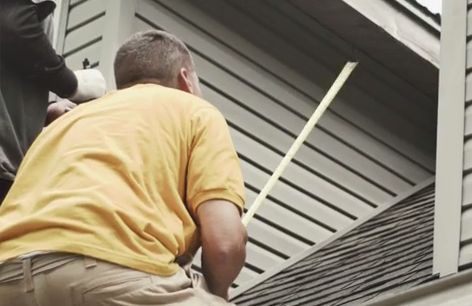 Two people installing siding on a house. One in yellow shirt holds a measuring tape.