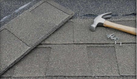 Roofing repair: Asphalt shingle next to a hammer and nails on a roof.