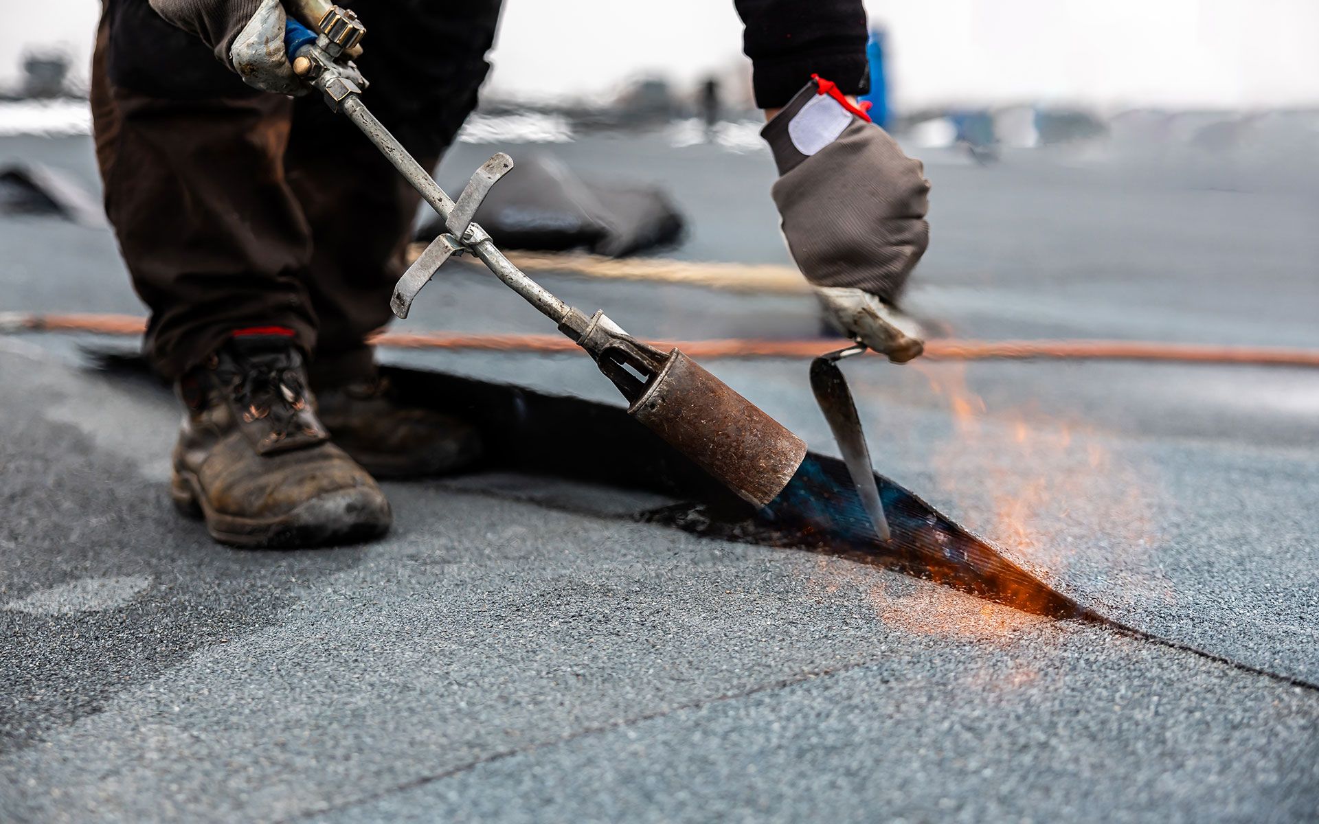Roofer using a torch to seal seams on a flat, black roof. Sparks and flames are visible.