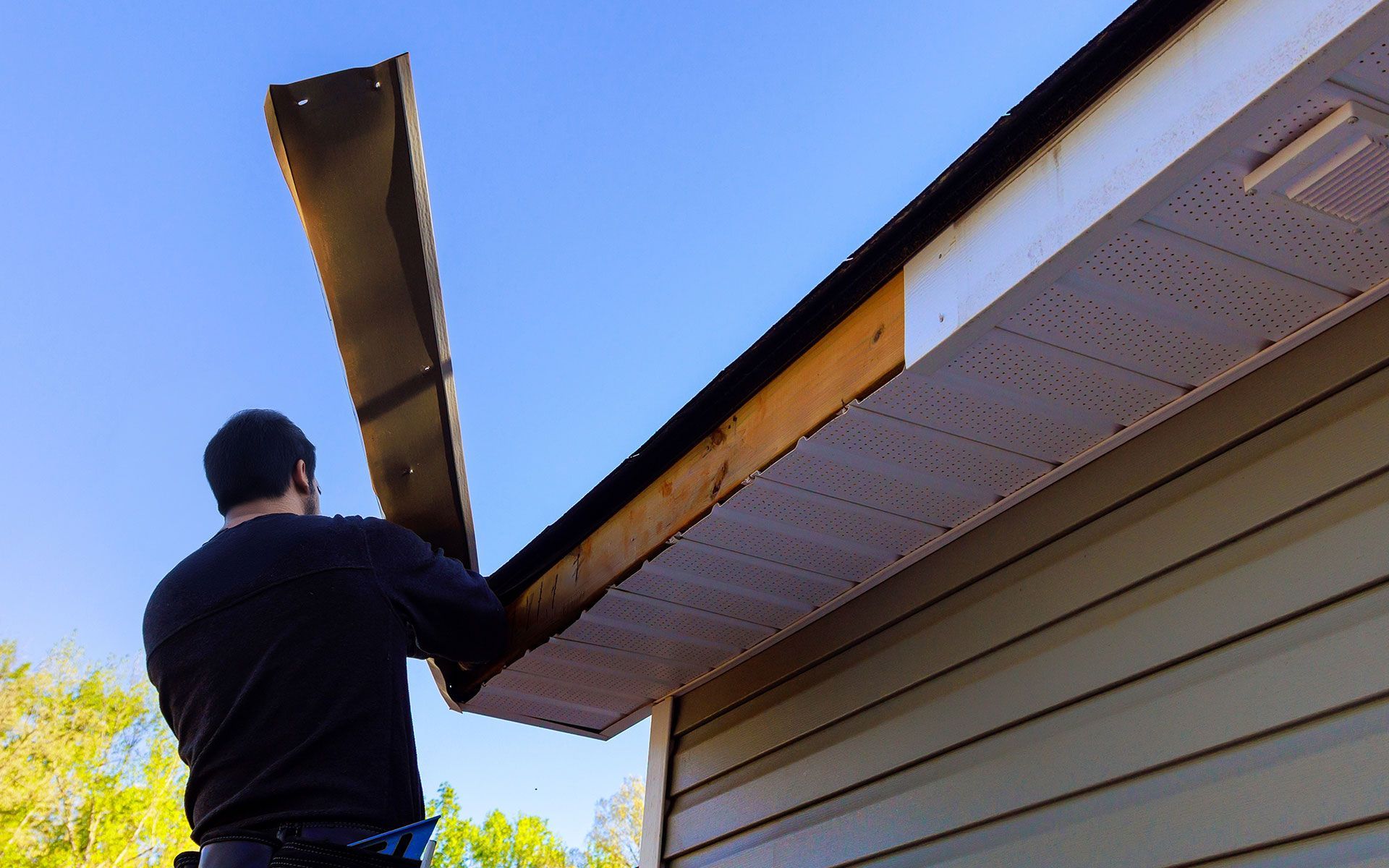 Man installing soffit on a house with a blue sky background.
