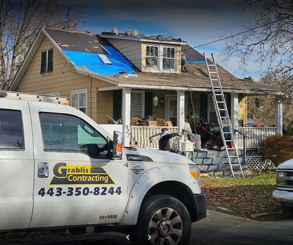 Roofer in safety gear installing gray tiles on a partially constructed roof.
