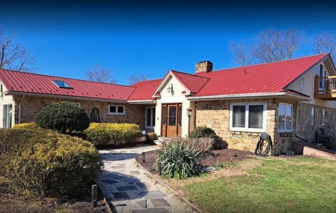 House with a red roof, stone facade, and a brick pathway leading to the front door, under a clear blue sky.